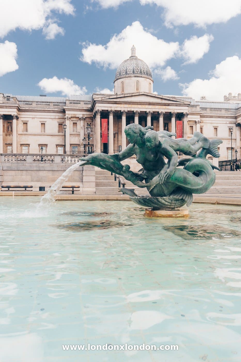 Bronze mermaid and dolphin fountain sculpture in Trafalgar Square with the National Gallery behind