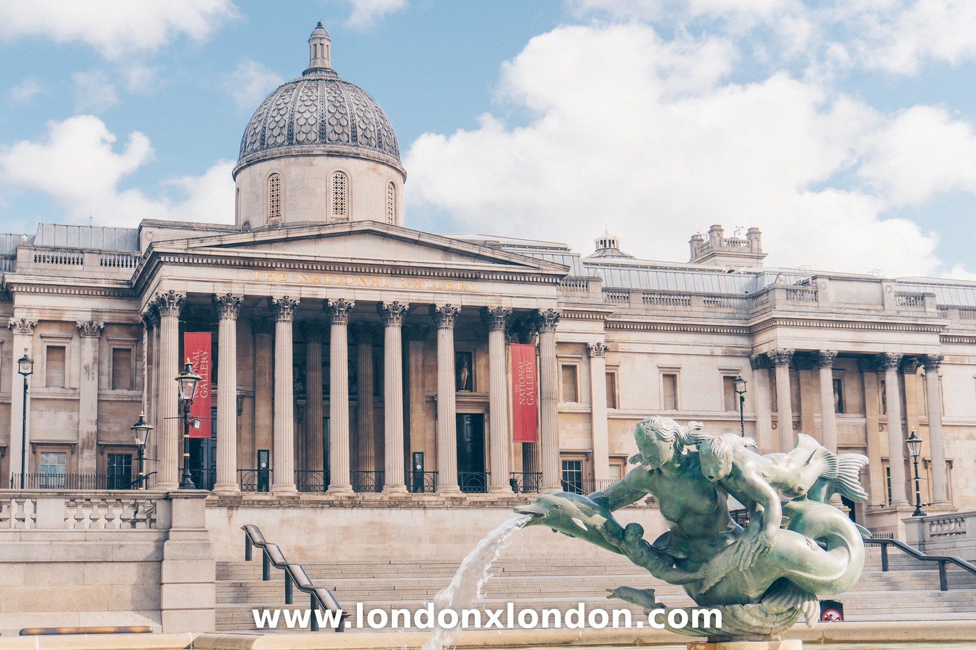 Wide view of Trafalgar Square fountains and the National Gallery steps on a sunny day