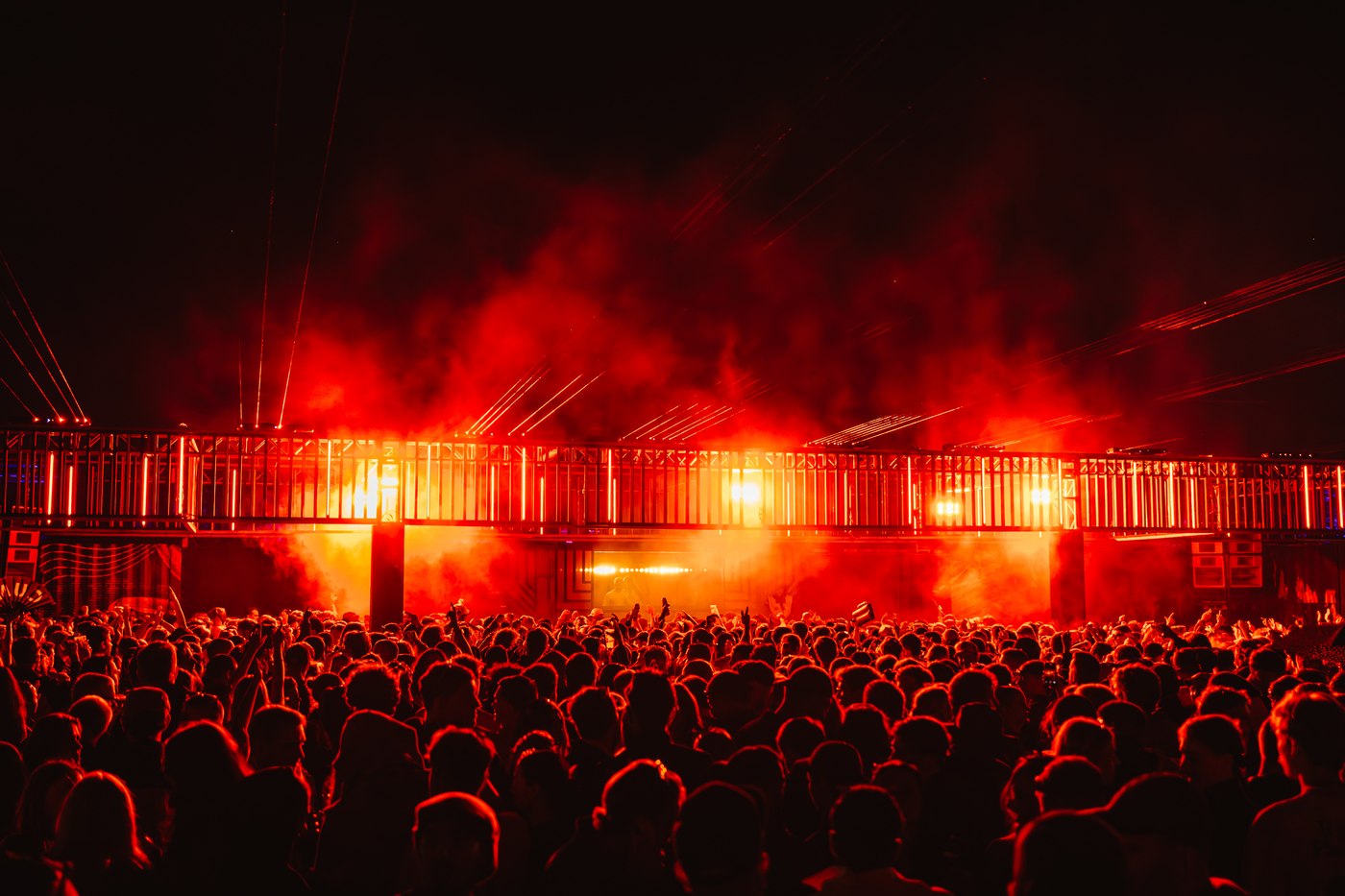 A dense festival crowd silhouetted in red light in front of a steel-framed stage at Waterworks