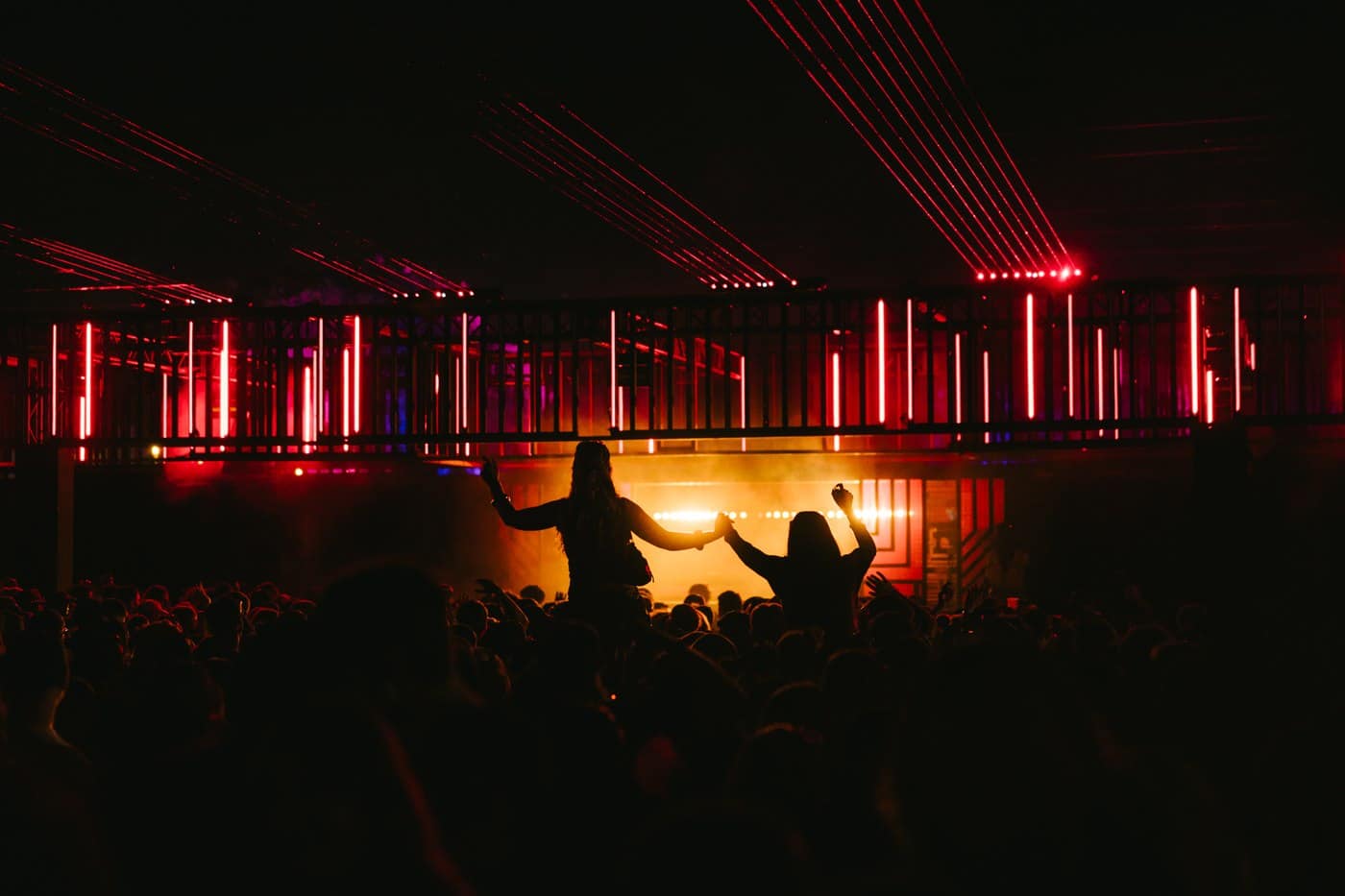 Two people raised on shoulders holding hands as red lasers fan out over a Waterworks stage